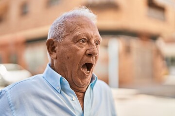Senior grey-haired man standing with surprise expression at street