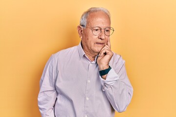 Senior man with grey hair wearing elegant shirt and glasses serious face thinking about question with hand on chin, thoughtful about confusing idea