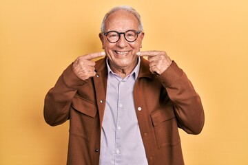 Senior man with grey hair wearing casual jacket and glasses smiling cheerful showing and pointing with fingers teeth and mouth. dental health concept.
