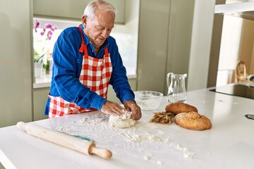 Senior man smiling confident keading dough with hands at kitchen
