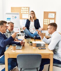 Businesswoman enjoys meditating during meeting. Sitting on desk near arguing partners at the office.