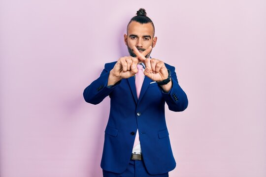 Young hispanic man wearing business suit and tie rejection expression crossing fingers doing negative sign