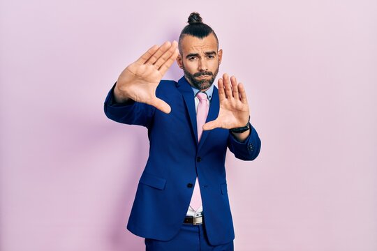 Young hispanic man wearing business suit and tie doing frame using hands palms and fingers, camera perspective