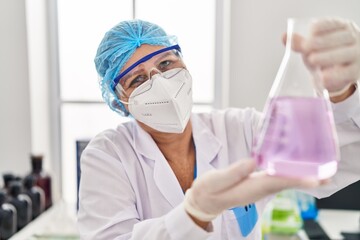 Middle age woman wearing scientist unifor and medical mask holding test tube at laboratory