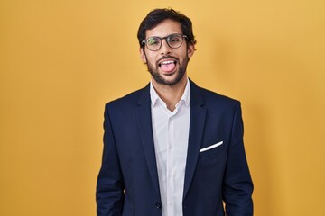Handsome latin man standing over yellow background sticking tongue out happy with funny expression. emotion concept.