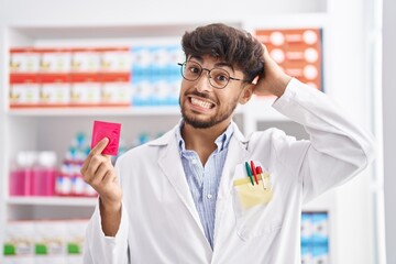 Arab man with beard working at pharmacy drugstore holding condom sticking tongue out happy with funny expression.