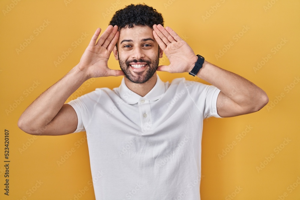 Sticker arab man standing over yellow background smiling cheerful playing peek a boo with hands showing face