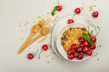 Summer breakfast concept. Healthy morning food. Ripe cherries and granola, light concrete background