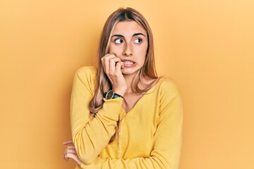 Beautiful hispanic woman wearing casual yellow sweater looking stressed and nervous with hands on mouth biting nails. anxiety problem.