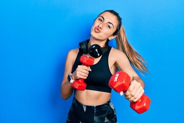 Beautiful hispanic woman wearing sportswear using dumbbells looking at the camera blowing a kiss being lovely and sexy. love expression.