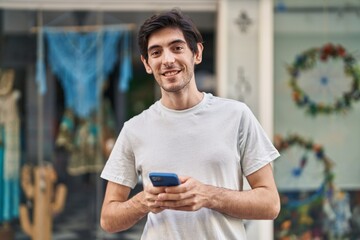 Young hispanic man smiling confident using smartphone at street