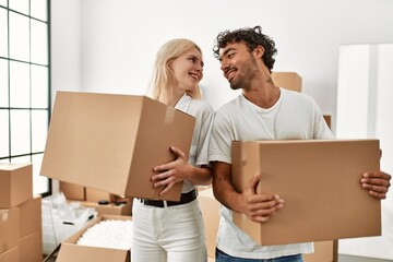 Young beautiful couple smiling happy holding cardboard boxes at new home.