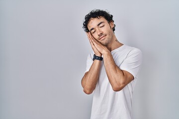 Hispanic man standing over isolated background sleeping tired dreaming and posing with hands together while smiling with closed eyes.