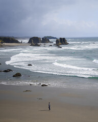 Man walking along a beach with a bay in the background