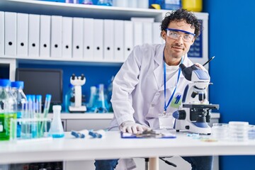 Fototapeta premium Young hispanic man scientist writing on document using microscope at laboratory