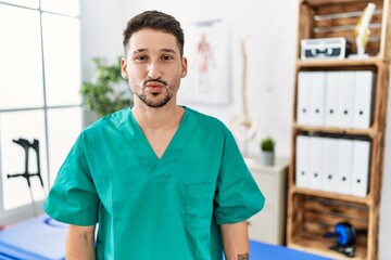 Young physiotherapist man working at pain recovery clinic looking at the camera blowing a kiss on air being lovely and sexy. love expression.