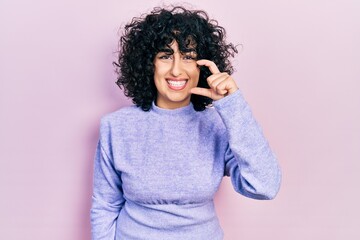 Young middle east woman wearing casual clothes smiling and confident gesturing with hand doing small size sign with fingers looking and the camera. measure concept.