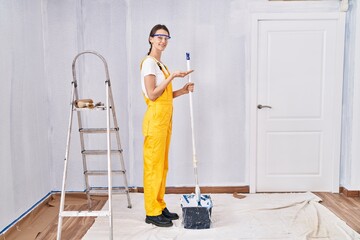 Young caucasian woman painting walls pointing aside with hands open palms showing copy space, presenting advertisement smiling excited happy