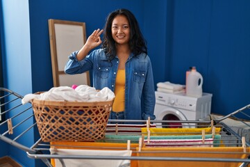 Young asian woman hanging clothes at clothesline smiling positive doing ok sign with hand and fingers. successful expression.
