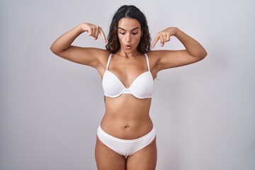 Fototapeta premium Young hispanic woman wearing white lingerie pointing down with fingers showing advertisement, surprised face and open mouth
