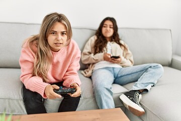 Girl playing video game and her girlfriend boring using smartphone at home.