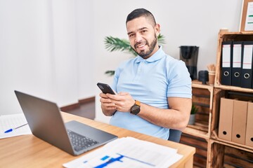 Young latin man business worker using laptop and smartphone at office
