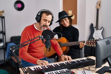 Fototapeta na wymiar Middle age man and woman musicians playing guitar and keyboard piano singing song at music studio