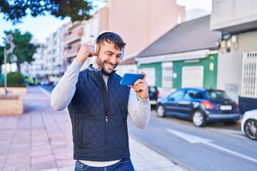 Young hispanic man smiling confident playing video game at street