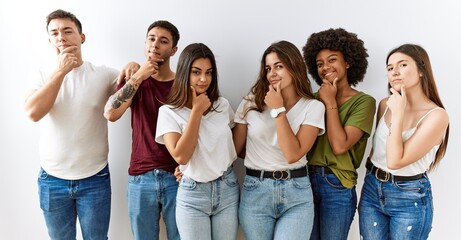 Group of young friends standing together over isolated background looking confident at the camera smiling with crossed arms and hand raised on chin. thinking positive.