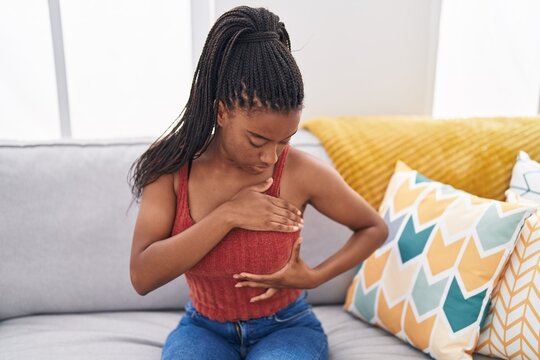African american woman examining breast with hand sitting on sofa at home