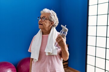 Senior grey-haired woman wearing sportswear holding water bottle at sport center