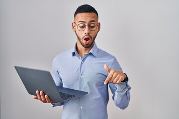 Young hispanic man working using computer laptop pointing down with fingers showing advertisement, surprised face and open mouth