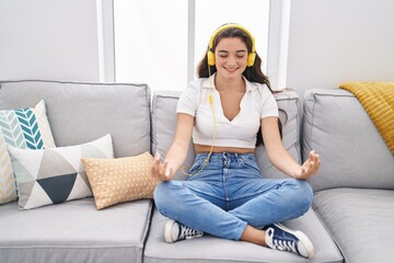 Young hispanic woman doing yoga exercise sitting on sofa at home