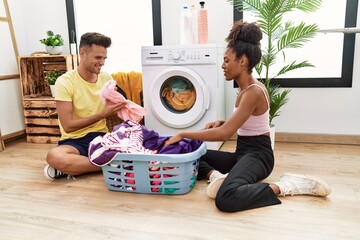 Man and woman couple smiling confident washing clothes at laundry room