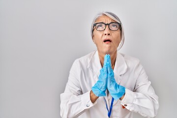 Middle age woman with grey hair wearing scientist robe begging and praying with hands together with hope expression on face very emotional and worried. begging.