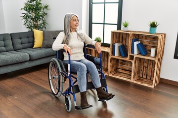 Middle age grey-haired woman smiling confident sitting on wheelchair at home