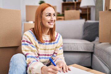 Young caucasian woman smiling confident writing on notebook at new home