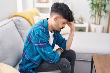 Young hispanic man stressed sitting on sofa at home