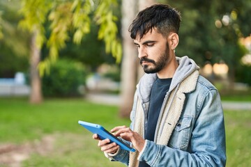 Fototapeta premium Young hispanic man using touchpad standing at park