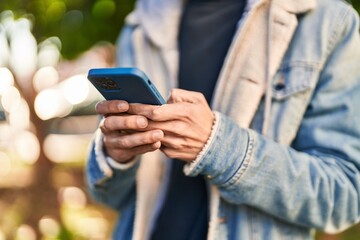 Young hispanic man using smartphone at park