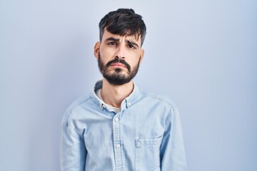 Fototapeta premium Young hispanic man with beard standing over blue background depressed and worry for distress, crying angry and afraid. sad expression.