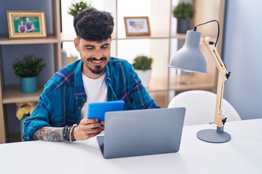 Young hispanic man using laptop and touchpad sitting on table at home
