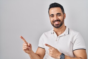 Young hispanic man with beard wearing casual clothes over white background smiling and looking at the camera pointing with two hands and fingers to the side.