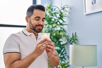 Young hispanic man smiling confident smelling candle at home