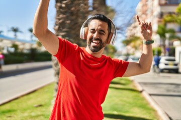 Young hispanic man listening to music and dancing at park