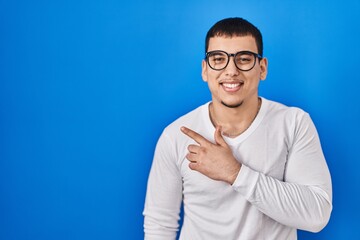 Fototapeta premium Young arab man wearing casual white shirt and glasses cheerful with a smile of face pointing with hand and finger up to the side with happy and natural expression on face