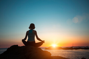 Naklejka premium A woman does yoga, meditating on an ocean beach during a beautiful sunset.