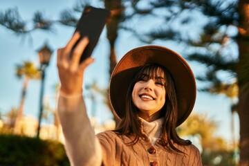 Brunette woman wearing winter hat taking a selfie picture with smartphone at the park