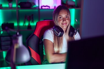 Young beautiful hispanic woman streamer sitting with arms crossed gesture at gaming room