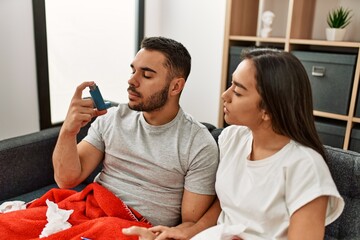 Young latin ill couple using inhaler sititng on the sofa at home.